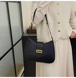 Close-up of minimalist black leather underarm bag with gold buckle on a stylish model