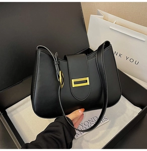Close-up of black leather shoulder bag with gold hardware, gift box and paper bag