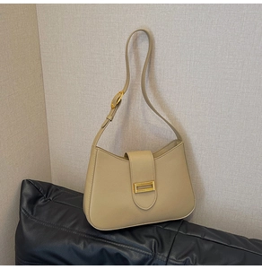 Close-up of beige shoulder bag featuring curved design and golden square buckle detail