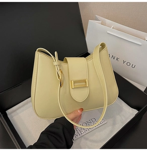 Detail of cream shoulder bag with golden square buckle next to luxury gift packaging