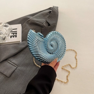 Blue shell-shaped acrylic clutch evening bag with gold chain strap on grey suit background