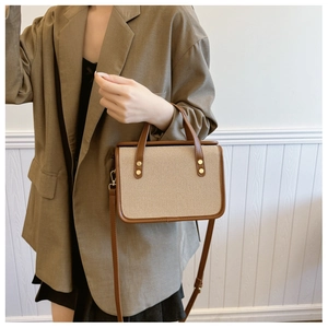 Detail of a vintage-style canvas crossbody bag with brown leather trim and metal buckles