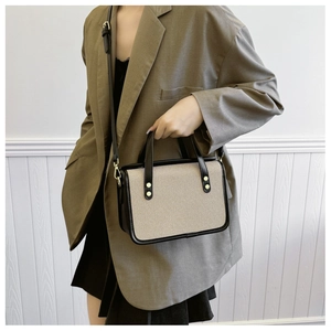 Detail of a minimalist canvas tote with black leather trim and gold rivet accents