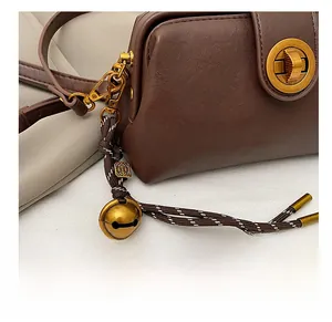 Detail of dark brown leather crossbody bag featuring a golden bell charm and twist lock