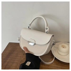 Detail of white leather and beige textured fabric patchwork on a saddle handbag with silver buckle