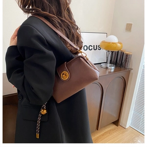 Close-up of a brown matte leather doctor-style bag with vintage gold clasp on black suit