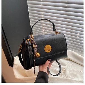 Detail of black leather satchel showing matte gold lock and woven pendant accessory