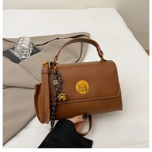 Detailed close-up of brown leather messenger bag with golden buckle and logo charm