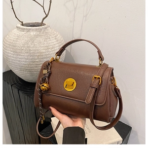 Detail of dark brown messenger bag with gold clasp and woven charm in a lifestyle setting