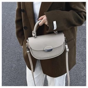 Close-up of beige shoulder bag with woven texture and oval metal clasp on street background