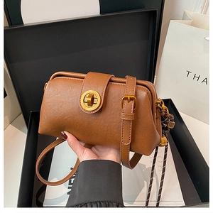 Close-up of vintage brown crossbody bag with gold clasp closure and woven pendant detail