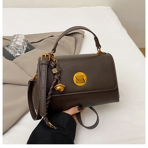 Detail of dark brown messenger bag featuring a golden clasp and braided rope charm pendant