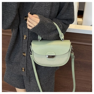 Detail of light green saddle bag featuring a textured flap and silver crescent buckle