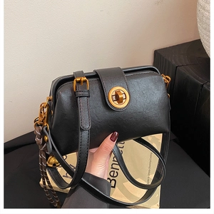 Detail of black crossbody bag with gold twist lock and woven bell charm accessory
