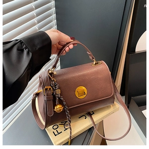 Detailed view of brown leather messenger bag with gold lock and woven charm detail