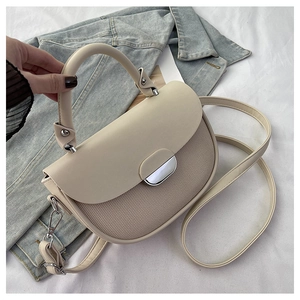 Detail of cream saddle bag featuring textured patchwork, metal lock, and round handle