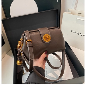 Detail of vintage matte brown shoulder bag featuring gold clasp and bell charm