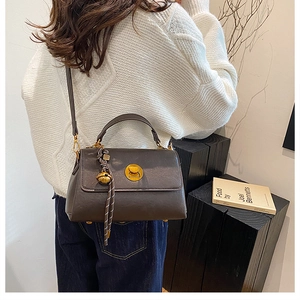 Detail view of dark brown messenger bag with gold twist lock on a stylish shoulder strap