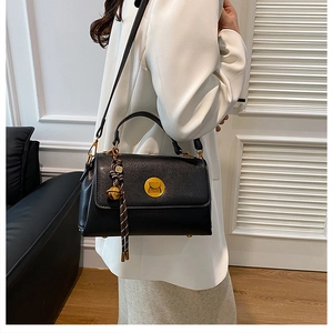 Detail of black PU leather messenger bag with gold circular buckle and woven tassel