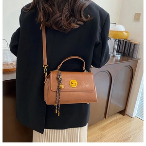 Detailed view of brown retro satchel with gold twist lock and woven tassel charm accessory