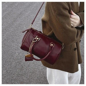 Detail of burgundy glossy Boston bag with mini charm and chain on model in brown coat