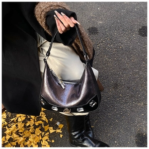 Detail of silver snake-pattern crescent bag with rhinestone embellishments on asphalt ground