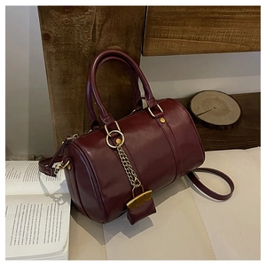 Detail of burgundy leather Boston bag featuring a gold chain lock charm and strap