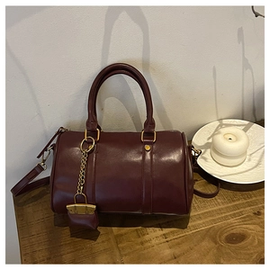 Detail of burgundy Boston bag with glossy finish and vintage gold chain on a wooden desk