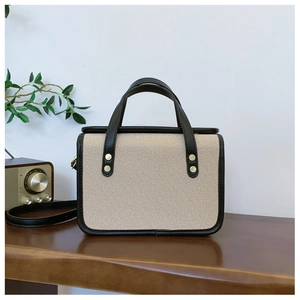 Minimalist cream canvas and black leather crossbody bag with top handles and gold rivets