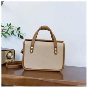 Minimalist canvas and leather crossbody bag with gold rivet accents on a wooden surface