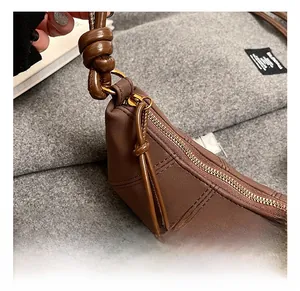 Close-up of golden zipper and knot detail on a dark brown leather hobo bag with stitching