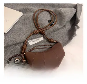 Detail of brown croissant bag with cream charm and strap on an aesthetic background