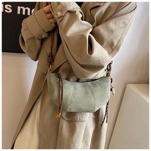Detail view of sage green crescent bag with decorative stitching and brown strap