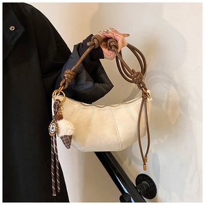 Detail of minimalist cream leather dumpling bag with brown knotted handle and plush charm