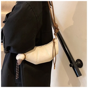 Close-up of white crescent crossbody bag with brown rope strap and fuzzy ball charm