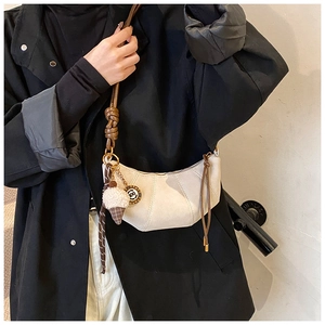 Detail of beige crescent bag with brown knotted strap and decorative charms on a model