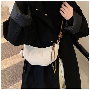 Detail of a minimalist half-moon crossbody bag with plush charm on a black winter coat