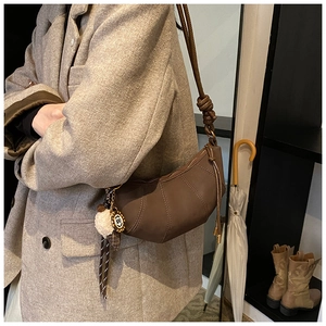 Detail of dark brown pleated dumpling bag with plush ice cream charm and metal tag