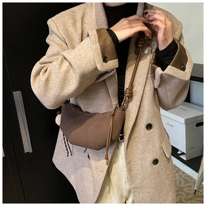 Brown croissant bag with pleated texture and pink pompom shown on a beige blazer