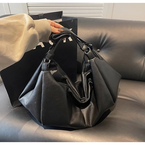 Detailed view of black pleated tote bag in litchi grain leather with wide shoulder strap