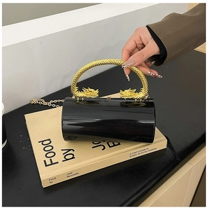 Detail of black acrylic clutch bag featuring textured gold double dragon handles and chain