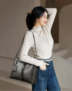 Detail of dark grey leather tote bag with tassels shown on a model in a modern interior
