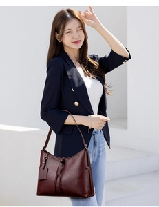 Detail of dark red leather handbag worn by a woman in a professional navy blazer and jeans