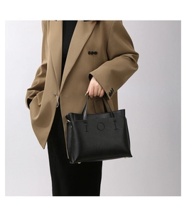 Detail of black pebbled leather tote bag with IOI embossed logo and metal bottom studs