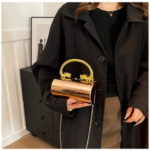 Detail of golden cylindrical clutch bag with dragon handles and polished mirror finish