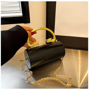 Detail of black acrylic cylindrical clutch with ornate gold dragon-shaped metal handle