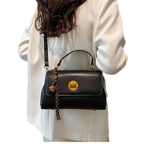Minimalist black leather messenger bag with gold hardware and bell tassel on white coat