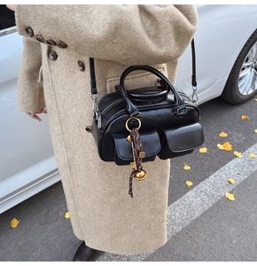 Close-up of black glossy leather Boston bag with decorative charms and twin front pockets