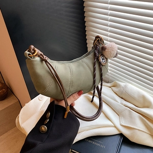 Green minimalist dumpling bag with knotted handle and plush charm shown in a lifestyle setting