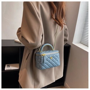 Detail of light blue quilted box bag featuring golden camellia logo and chain strap